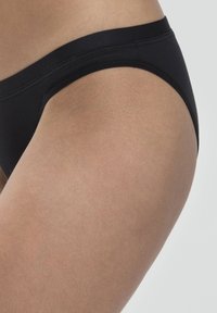 Slip in cotone nero con finitura liscia, dotato di un ampio elastico in vita e una taglia bassa, che mette in risalto il tono della pelle sulla coscia.