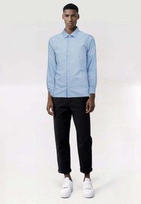 Camisa de botones azul claro con manguitas largas, combinada con pantalones negros ajustados y zapatillas blancas. La camisa presenta un diseño de cuello clásico.