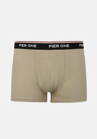 Beige herreboxershorts med sort talje, hvor der står "Pier One" i hvid skrift, vist fladt mod en neutral baggrund.