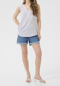 Top sin mangas de rayas blancas con escote en V, combinado con shorts de mezclilla enrollados. El calzado consiste en sandalias blancas de tacón cuadrado.
