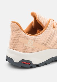 Salomon löparskor i ljus persikofärgad mesh med orange detaljer, med en strukturerad yta och en kontrasterande svart gummisula av Contagrip.