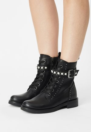 Černé kožené kotníkové boots s krajkovým zapínáním, cvokovými akcenty, páskem s dekorativními perlami a texturovaným bočním panelem.