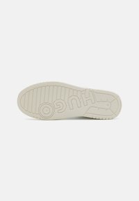 White rubber sneaker sole with textured grip, featuring "HUGO" embossed. Circular and ridged patterns enhance traction and design detail.