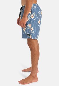 Pánske plavky v svetlomodrom textile s kvetinovým vzorom v krémovej a červenej farbe. Obsahujú elastický pás a postrannú značku.