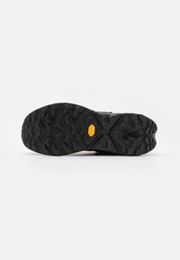 Fekete gumi talp mély barázdákkal és sárga Vibram díszítéssel, amely kontúros formával rendelkezik a tapadás és a stabilitás érdekében különböző felületeken.