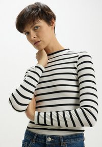 Maglietta a maniche lunghe a righe bianche e nere realizzata in tessuto a coste, con un design aderente e un collo alto.