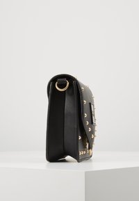 Borsa a tracolla in pelle nera con accenti a borchie dorate, forma rettangolare e un anello laterale per il fissaggio. Texture liscia, design minimalista.