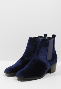 Botines de terciopelo azul marino con un diseño elegante, paneles laterales elásticos y un tacón bajo en bloque. Textura suave con un acabado pulido.