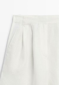 Pantaloni bianchi a vita alta con pieghe e tasche laterali, realizzati in tessuto strutturato.