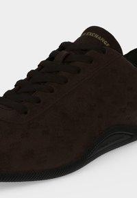 Baskets en daim brun foncé avec lacets noirs, semelle texturée et texte "ARMANI EXCHANGE" sur la languette rembourrée.