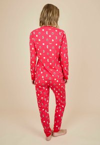 Conjunto de pijama rojo con mangas largas y pantalones, que presenta un patrón juguetón de juguetes y decoraciones. La tela parece suave con puños acanalados.
