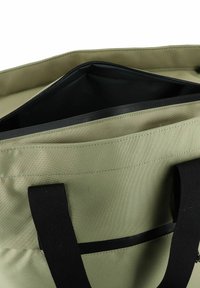 Een groene stoffen draagtas met zwarte handvatten, met een open rits die een zwarte binnenkant onthult en een voorvak detail. Getextureerd materiaal.