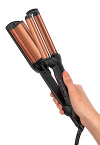 Mano che tiene un arricciacapelli a triplo cilindro nero e rame con interruttore di accensione e cavo su sfondo bianco.