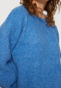 Blue knitted sweater made of soft, textured fabric. Features a round neckline and relaxed fit. Cozy appearance with subtle variations in hue.