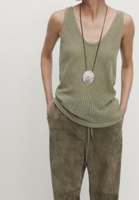 Olive green knit tank top with a loose fit and scoop neckline, paired with matching olive suede drawstring pants. Circular metallic pendant necklace.