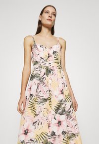 Florales Maxikleid in Rosa und Gelb mit Blättermustern, mit dünnen Trägern und einer Knopfleiste vorne, aus leichtem Stoff gefertigt.