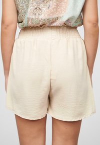 Shorts beiges en matière douce, dotés d'une taille élastique et d'une coupe décontractée, avec un ourlet qui remonte légèrement.