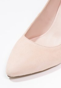 Escarpin en suede nude à talon haut, avec un bout pointu et un décolleté bas. Texture lisse avec un léger brillant et un design simple et épuré.