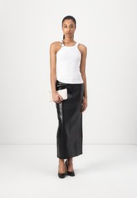 Witte geribbelde tanktop met een zilveren accent, gecombineerd met een zwarte leren maxirok. Houdt een textuur clutch in roomkleur vast. Zwarte pumps.
