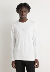 Camiseta de manga longa branca em algodão, com decote redondo e pequeno logotipo preto "BOSS" no centro do peito.