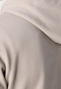 Sudadera de algodón beige con una textura suave y un corte relajado. Los detalles notables incluyen una capucha y puños acanalados.