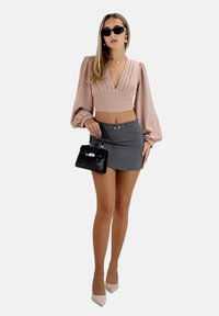 Helles rosa kurzes Blusenshirt mit Falten, grauer Minirock, schwarze Handtasche und beigefarbene spitze Absätze, accessoriert mit Sonnenbrille und Ohrringen.