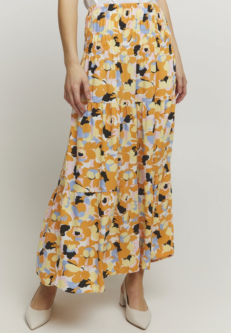 Verboden maxi rok in oranje, geel en blauw met een smocked tailleband. Kenmerkt tiered lagen en een vloeiende stijl, gecombineerd met beige hakken.
