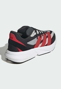Čierne a červené športové topánky majú sieťovanú vrchnú časť s šedými akcentmi, ľahkým bielym profilom a čiernou gumovou podrážkou pre lepšiu trakciu.