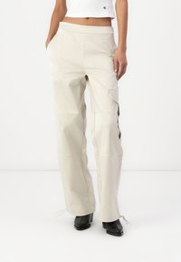 Pantaloni cargo beige chiaro a gamba larga con una texture liscia, dotati di tasche laterali e legature regolabili all'orlo. Realizzati in materiale leggero.