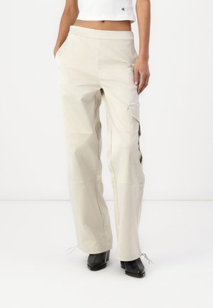 Pantalones cargo de pierna ancha en color beige claro, con una textura suave, que cuentan con bolsillos laterales y lazos ajustables en el dobladillo. Fabricados con material liviano.
