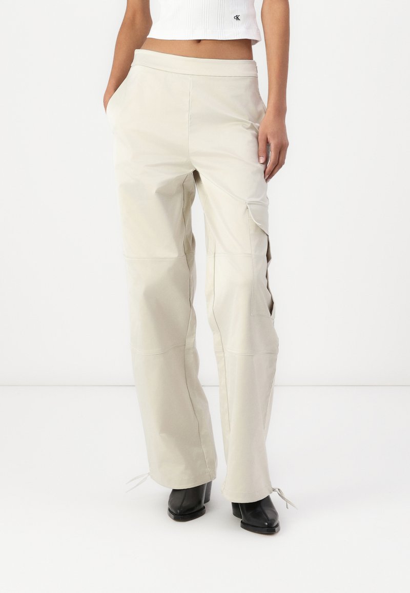 Pantaloni cargo beige chiaro a gamba larga con una texture liscia, dotati di tasche laterali e legature regolabili all'orlo. Realizzati in materiale leggero.