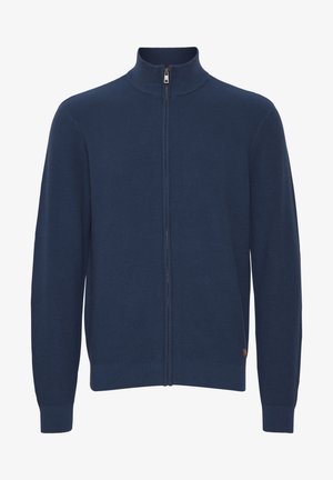 Námornícky modrý zipsový sveter s ryhovanou textúrou, vysokým golierom a priliehajúcimi manžetami. Obsahuje jemný akcent loga na dolnej strane.