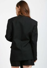 Schwarzer, taillierter Blazer mit strukturiertem Schnitt, Ein-Knopf-Verschluss und Schulterpolstern. Glattes Material mit matter Oberfläche.