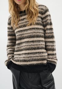 Raidallinen neulebeige, musta ja harmaa. Pehmeä tekstuuri, pyöreä pääntie ja ribbaatut mustat hihansuut, yhdistetty tummiin laskostettuihin housuihin.