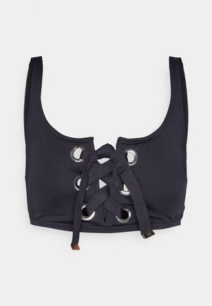 Svart badetopp med lisseopplegg i front og sølvfargede metallringer, brede skulderstropper og en glatt, stretchy tekstur.