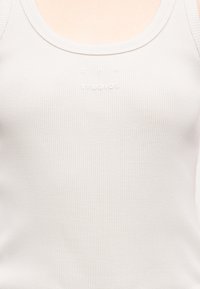 Λευκό ριμπ αμάνικο με διακριτικό ανάγλυφο λογότυπο "A.P.C. Studios" κεντραρισμένο στο στήθος.