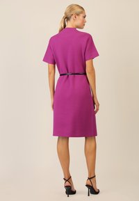 Vestido rosa a la altura de la rodilla con mangas cortas, ajustado a la cintura con un cinturón negro. Textura suave, escote redondo y diseño simple.