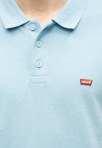 Polo bleu clair avec trois boutons et un petit patch logo rouge Levi's sur la partie gauche de la poitrine.