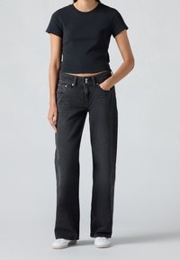 T-shirt noire raccourcie associée à un jean sombre taille haute à jambes larges. Comprend un design classique à cinq poches et une fermeture à boutons argentés. Baskets blanches.