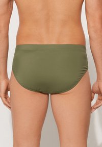 Zelené plavecké boxerky s bezešvým designem, elastickým pasem a hladkým povrchem. Mají nízký střih na zadní straně pro minimální zakrytí.