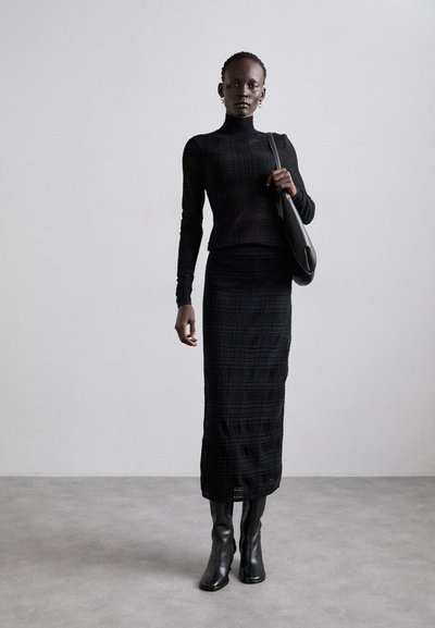 Svart långärmad stickad topp med hög hals och figurnära silhuett, tillsammans med en svart texturerad midikjol och knähöga svarta stövlar.