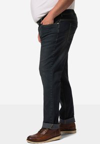 Jeans in denim scuro con taglio dritto, risvolti e design classico. Presenta due tasche laterali e cuciture a contrasto. Scarpe stringate marroni.