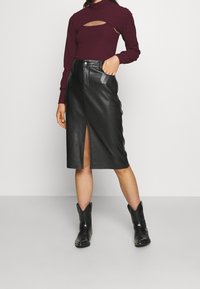 Svart läder midi kjol med framknäppning, i kombination med en vinröd ribbad långärmad topp med ett utskuret mönster. Svarta cowboystövlar.