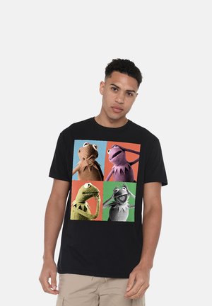 Junger Mann trägt ein schwarzes T-Shirt mit vier bunten Feldern, die jeweils Kermit den Frosch in verschiedenen Posen und Ausdrücken zeigen.