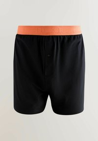 Melnas bokseršortus, kas izgatavoti no mīkstas auduma ar gludu tekstūru, ar oranžu elastīgu jostu, uz kuras ir izdrukāts vārds "NEXT" sietiņu rakstā.