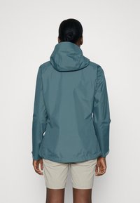 Vattentålig grönblå jacka med huva, figursydd design och elastiska ärmslut; har en slät yta och minimalistisk stil.