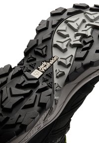 Suola di scarpa da trekking nera con battistrada in gomma texturizzata, caratterizzata da un logo prominente e da una miscela di motivi angolari e curvi per una migliore aderenza.