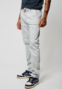 Pantalones de mezclilla gris claro con cintura con cordón, ajuste relajado y bolsillos laterales, combinados con zapatillas deportivas en tonos navy y crema.