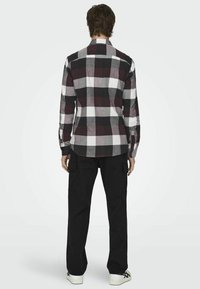 Camisa de cuadros en negro, blanco y burdeos con mangas largas y collar button-down, combinada con pantalones cargo negros y zapatillas blancas.