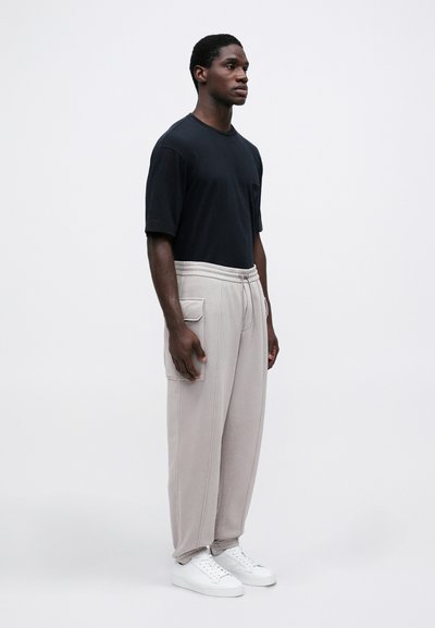 Μαύρο βαμβακερό μπλουζάκι, άνετη εφαρμογή; ανοιχτό γκρι φόρμες με πλαϊνές τσέπες και κορδόνι στη μέση; λευκά αθλητικά παπούτσια. Μινιμαλιστικός σχεδιασμός.